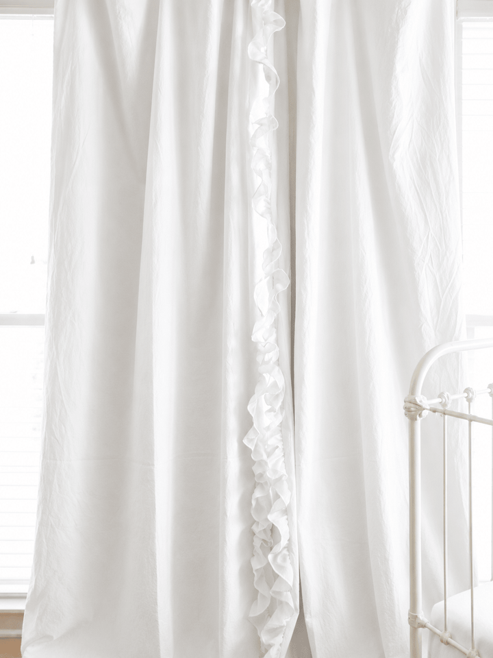 White ruffled blackout nursery curtains hanging beside a white crib, ruffle running down the leading edge of each panel - High Cotton Textile