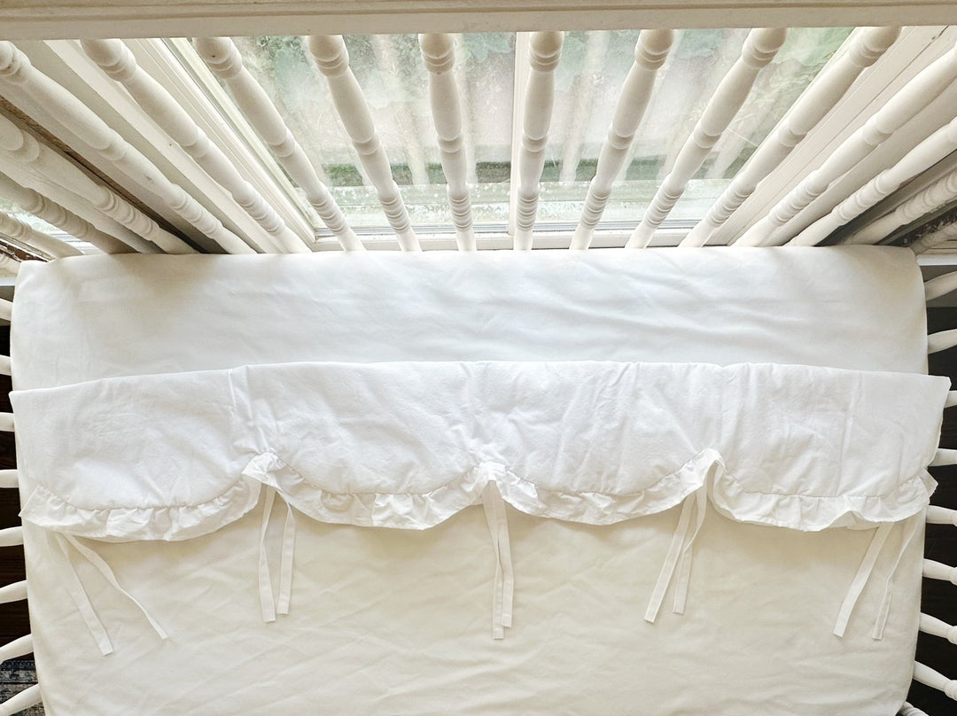 White ruffled crib rail cover shown from above across the long rail with cotton ties hanging loose
