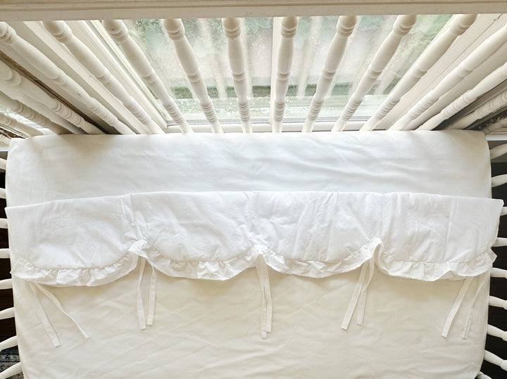 White ruffled crib rail cover shown from above across the long rail with cotton ties hanging loose