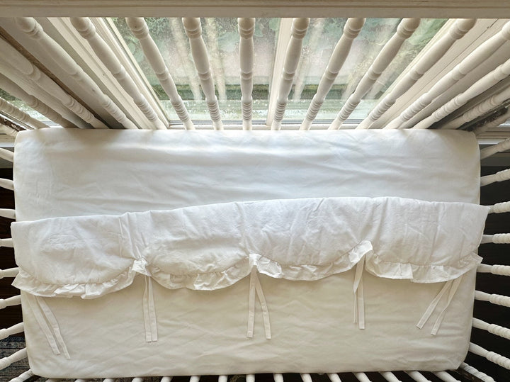 Overhead view of the white scalloped crib rail cover showing the scalloped hem and evenly spaced ties