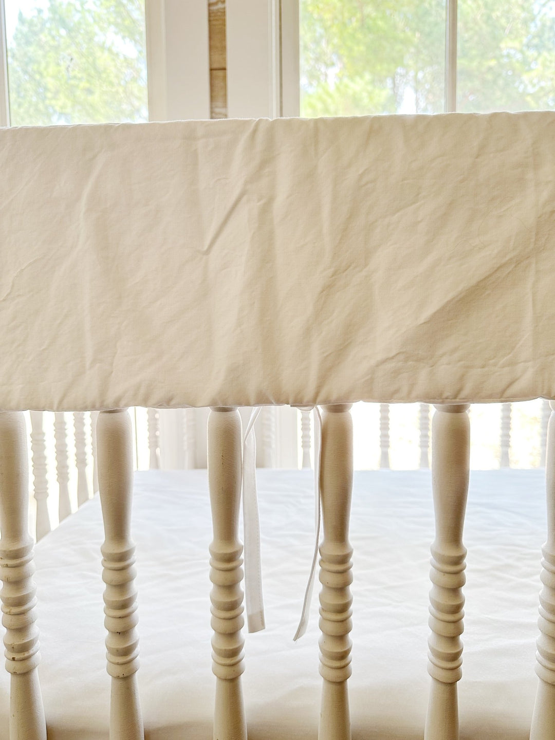 Monogrammed white rail cover seen from the front of the crib with ties hanging between spindles