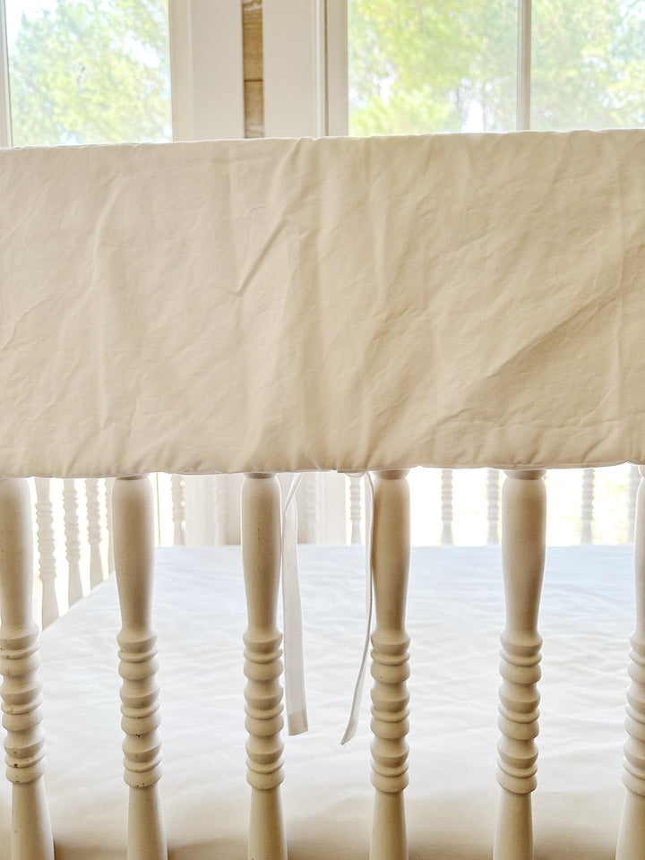 Monogrammed white rail cover seen from the front of the crib with ties hanging between spindles