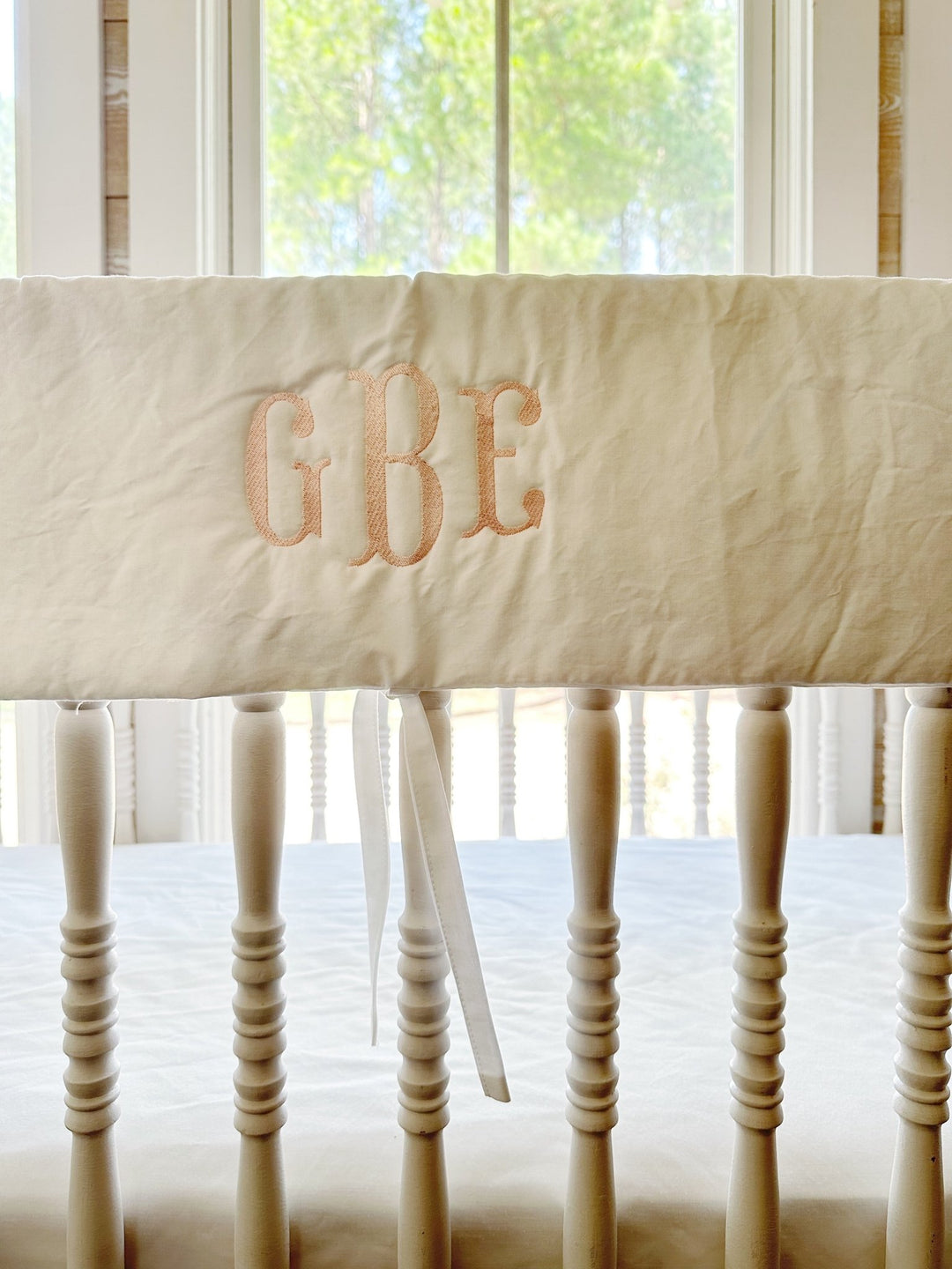 Close view of the pink three-letter monogram stitched on the white cotton rail cover