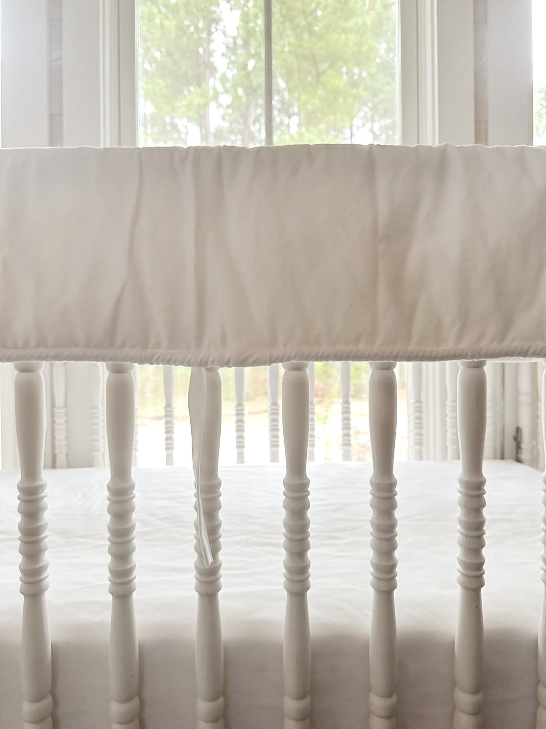 Close view of the white cording trim and a single tiny white tie against the turned crib spindles