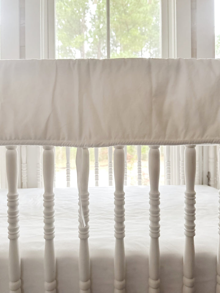 Close view of the white cording trim and a single tiny white tie against the turned crib spindles
