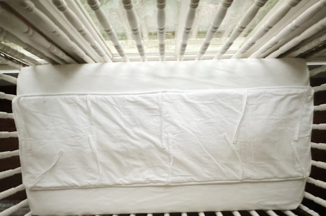 White tailored rail cover seen straight on across the front crib rail, cording visible along the lower edge