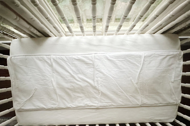 White tailored rail cover seen straight on across the front crib rail, cording visible along the lower edge